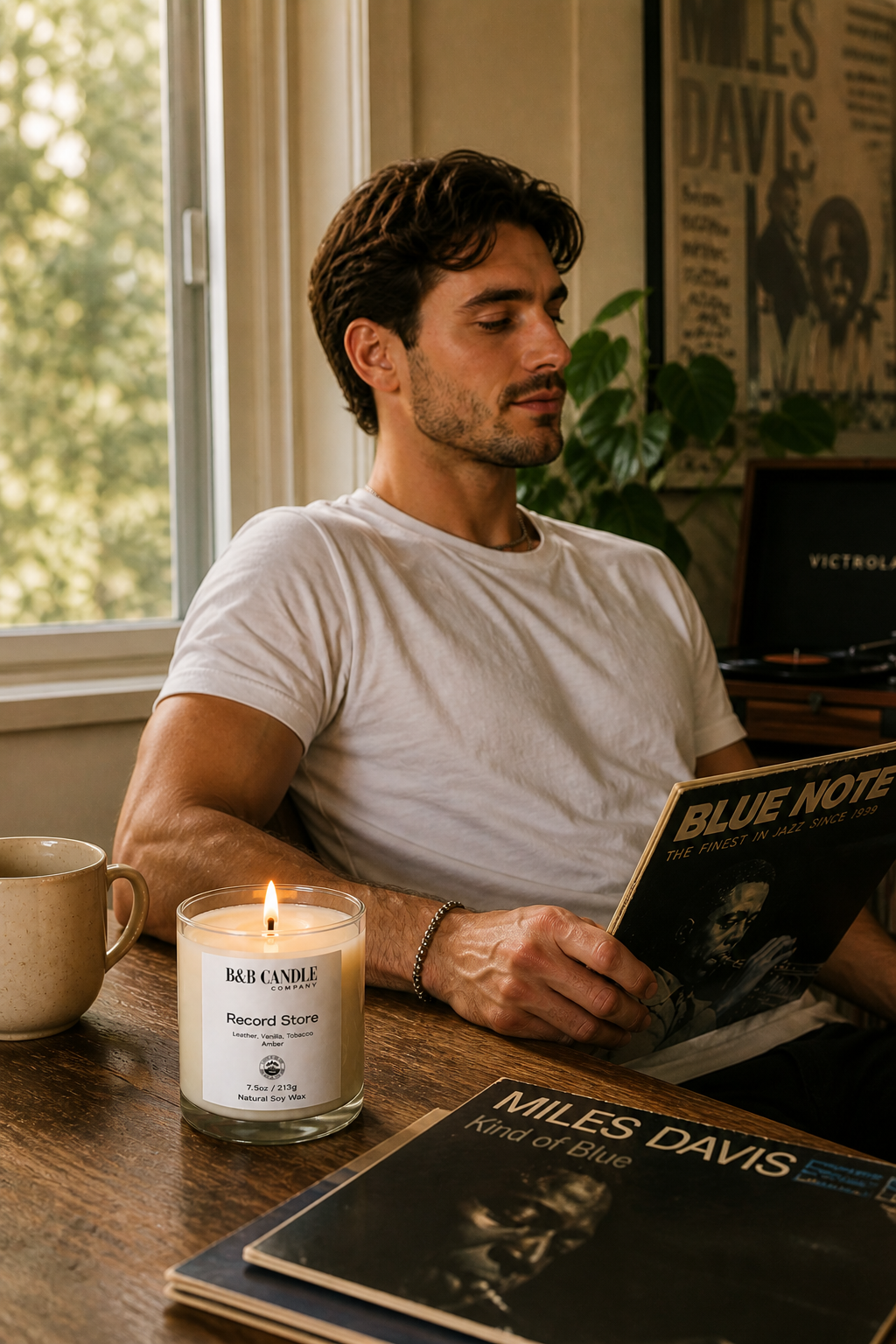Man reading a Blue Note record album with a lit candle and coffee mug on a table.