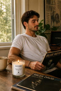 Man reading a Blue Note record album with a lit candle and coffee mug on a table.