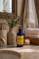 Bottle of B&B Candle Co. product on a bathroom counter with a candle and plant in the background.