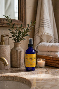 Bottle of B&B Candle Co. product on a bathroom counter with a candle and plant in the background.