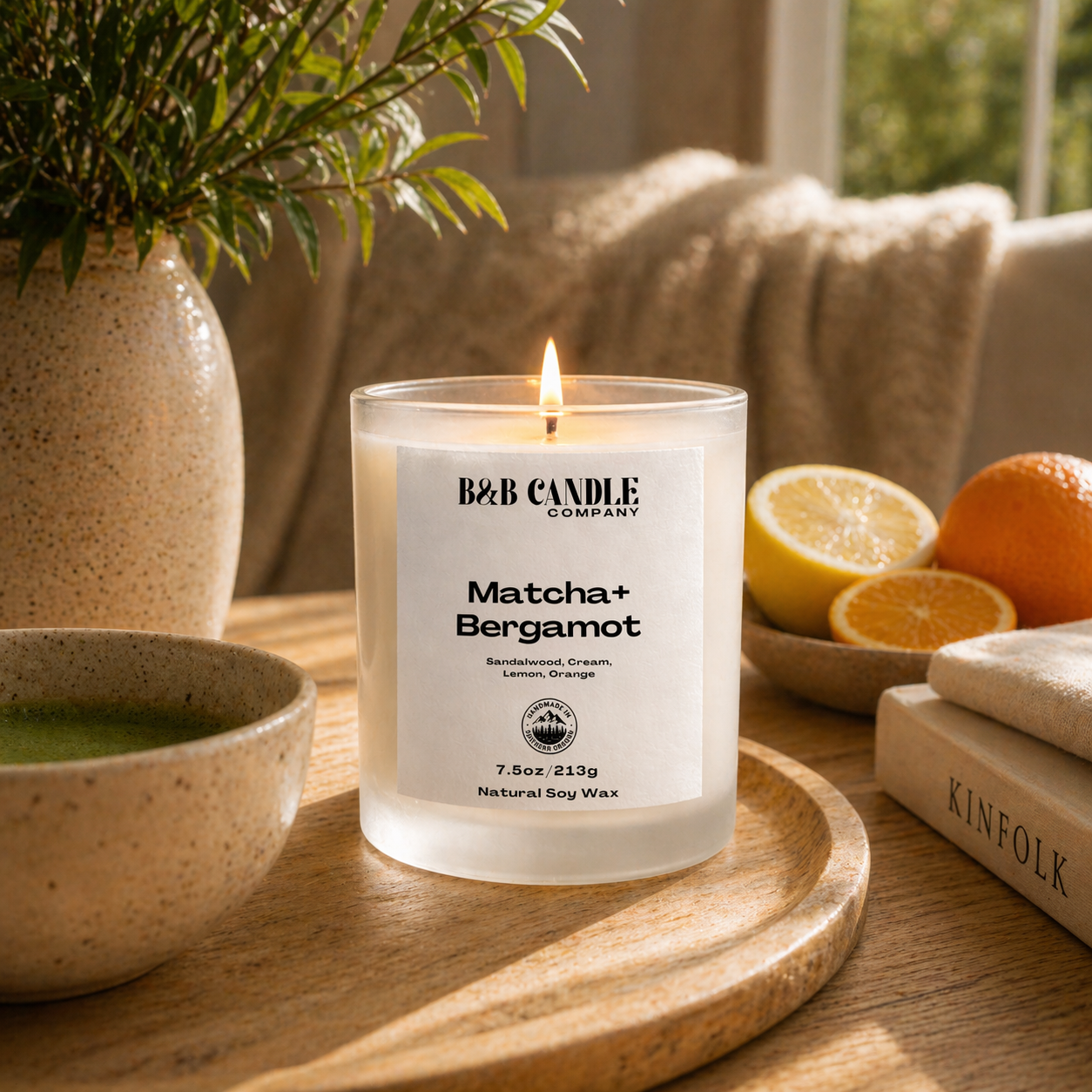 B&B Candle Company matcha bergamot candle on a wooden tray with a plant, bowl, and books in the background.