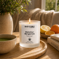 B&B Candle Company matcha bergamot candle on a wooden tray with a plant, bowl, and books in the background.