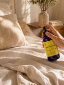 Hand holding a bottle of room spray product on a bed with soft lighting